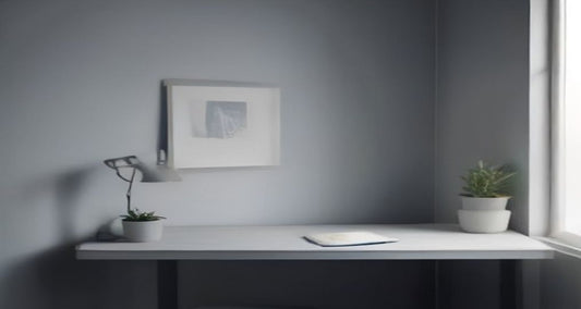 A quiet desk set against a pale grey wall, with a small plant and soft window light falling from the side.