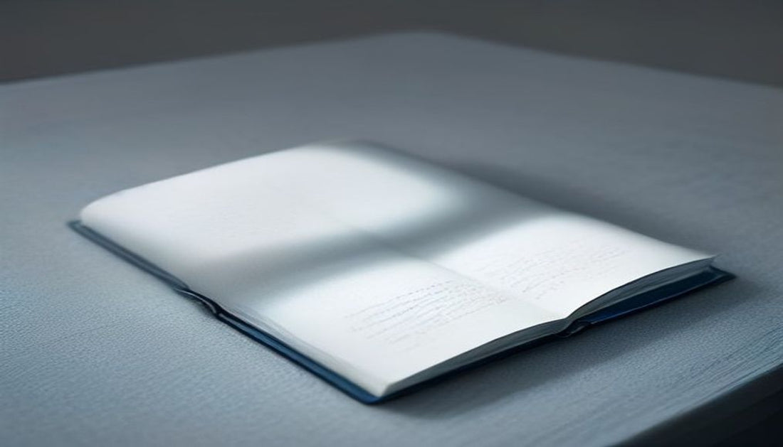 A pair of reading glasses resting on a closed notebook in soft cool blue-grey light, suggesting eyes at rest.