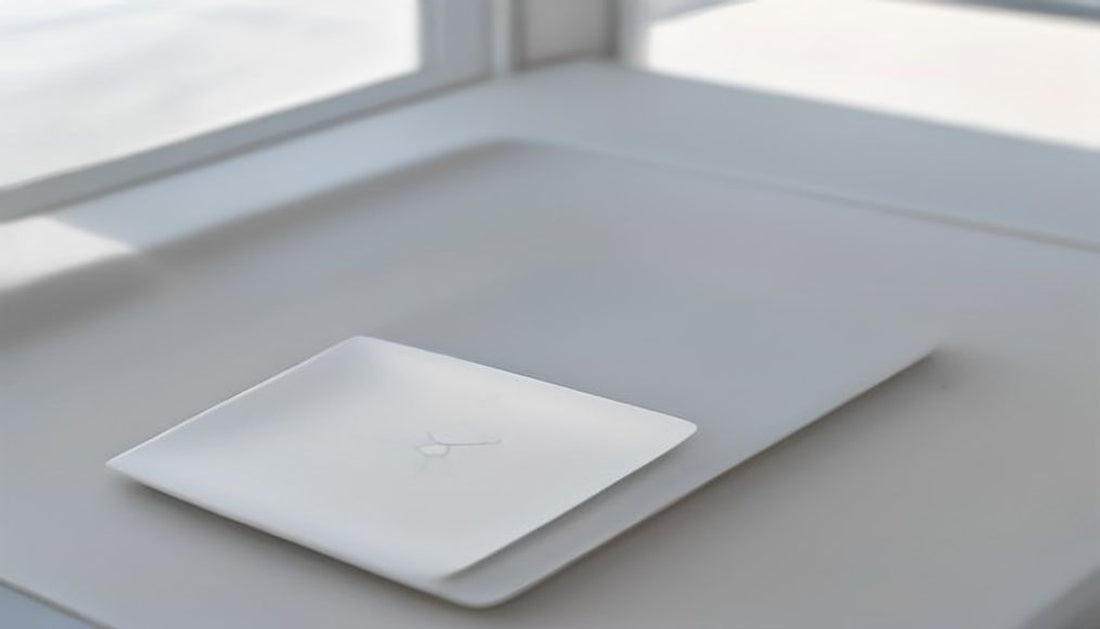 A small pale ceramic tray on a bright, clean desk holding keys, earbuds, and a slim pen.