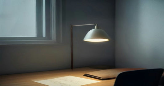 A desk lamp glowing over a blank card on a cleared wooden desk beside a dim early-morning window.