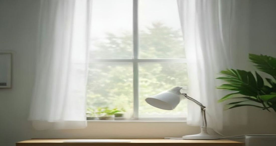 A bright home office corner with a white desk lamp on a wooden desk beside a window with sheer curtains and a leafy plant.