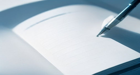 An open blank notebook with a pen resting across the page in soft blue window light.