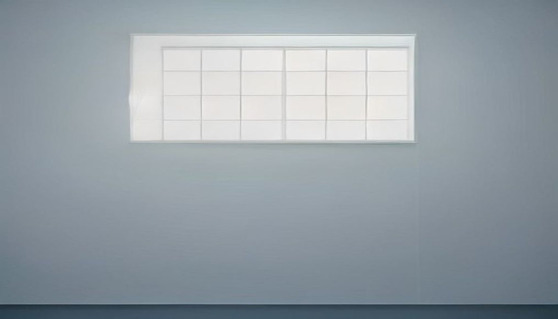 A minimalist wall calendar with blank squares on a pale grey-blue wall in soft directional light.